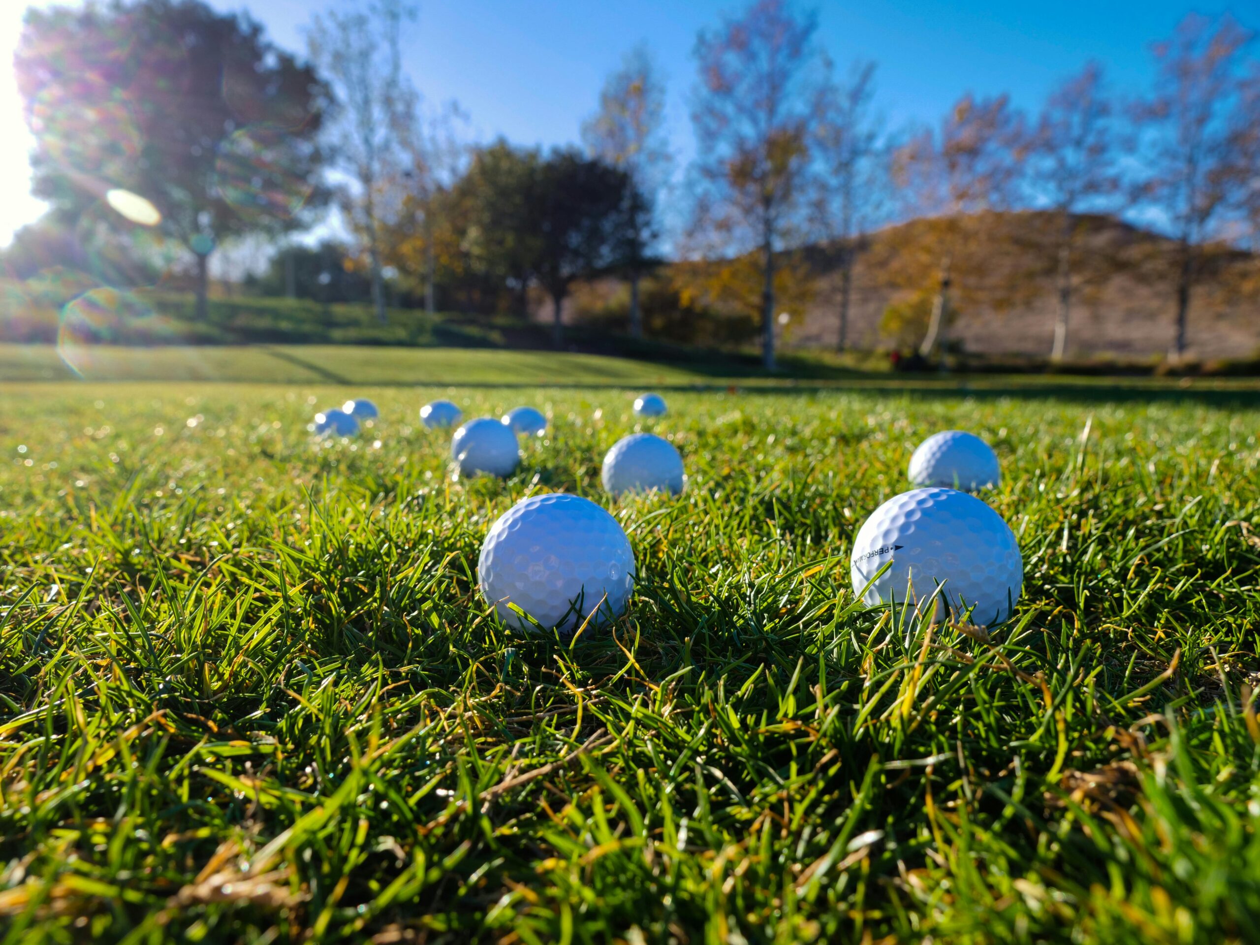Golf balls scattered on a lush green course under a clear blue sky.